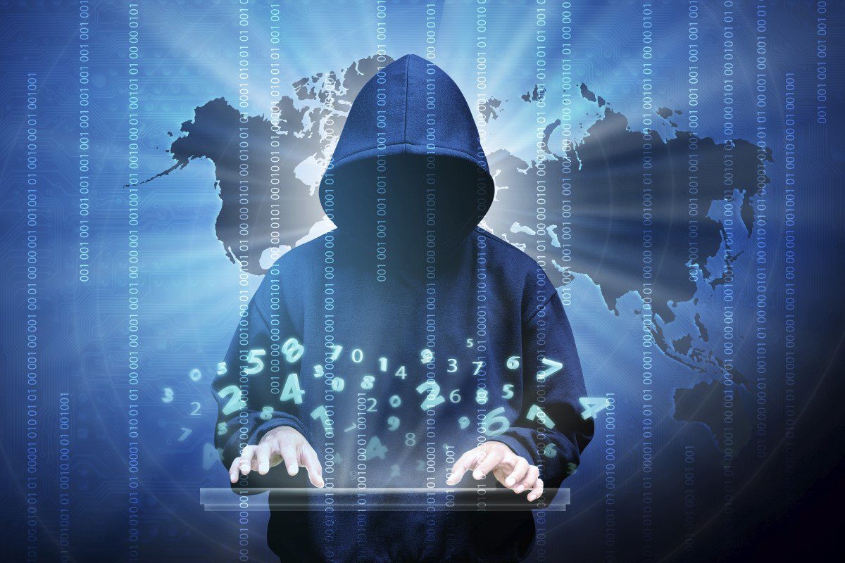 hooded hacker typing at computer with background of the world map
